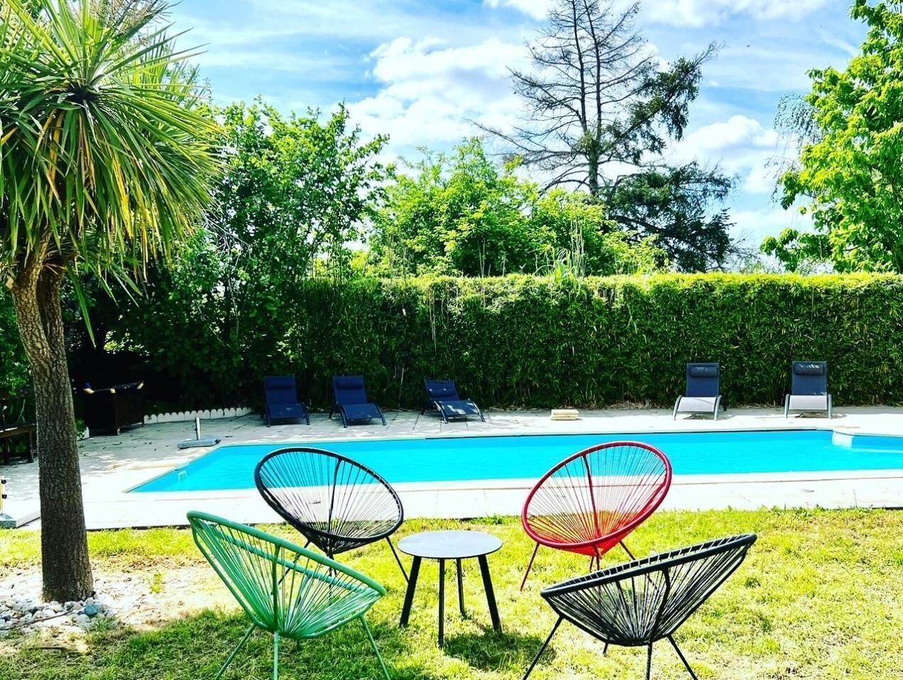 Une piscine avec des chaises longues et une petite table, le tout situé dans un espace verdoyant.