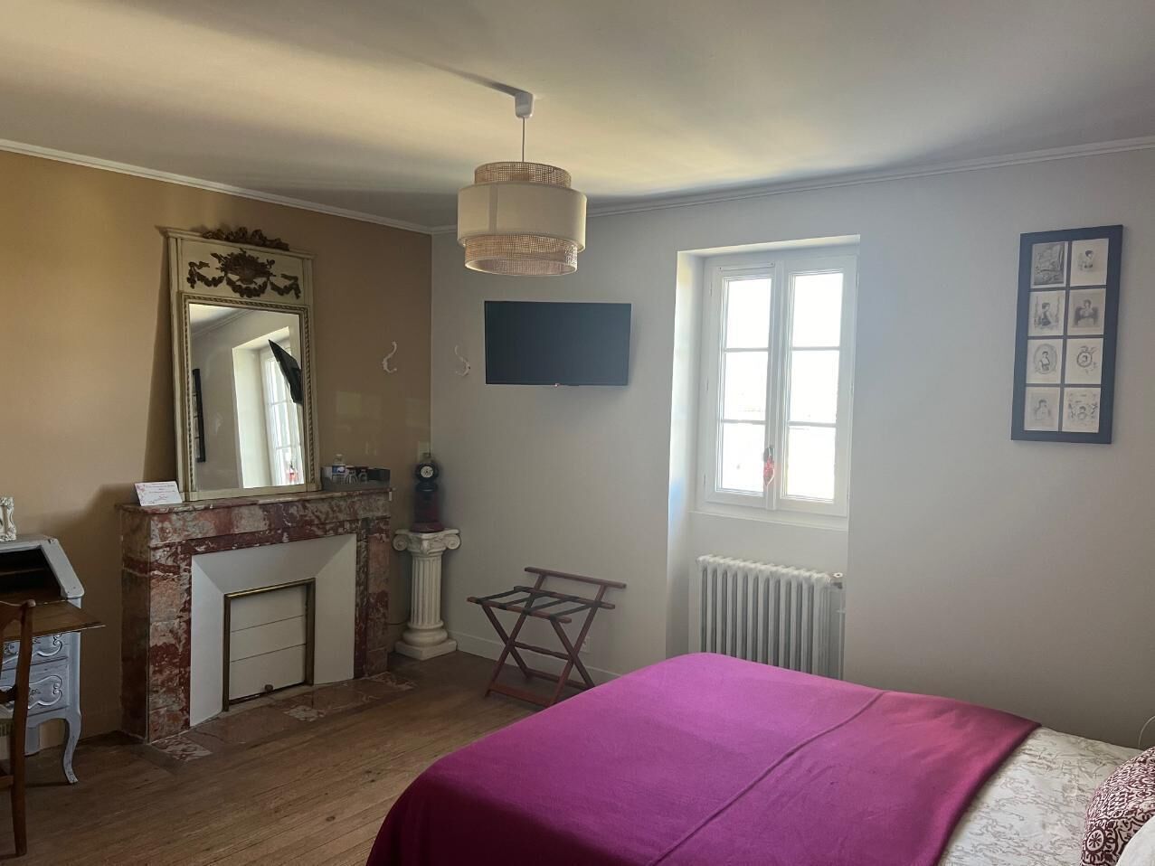 A bedroom with a bed, a fireplace, a mirror, a radiator, and a window.
