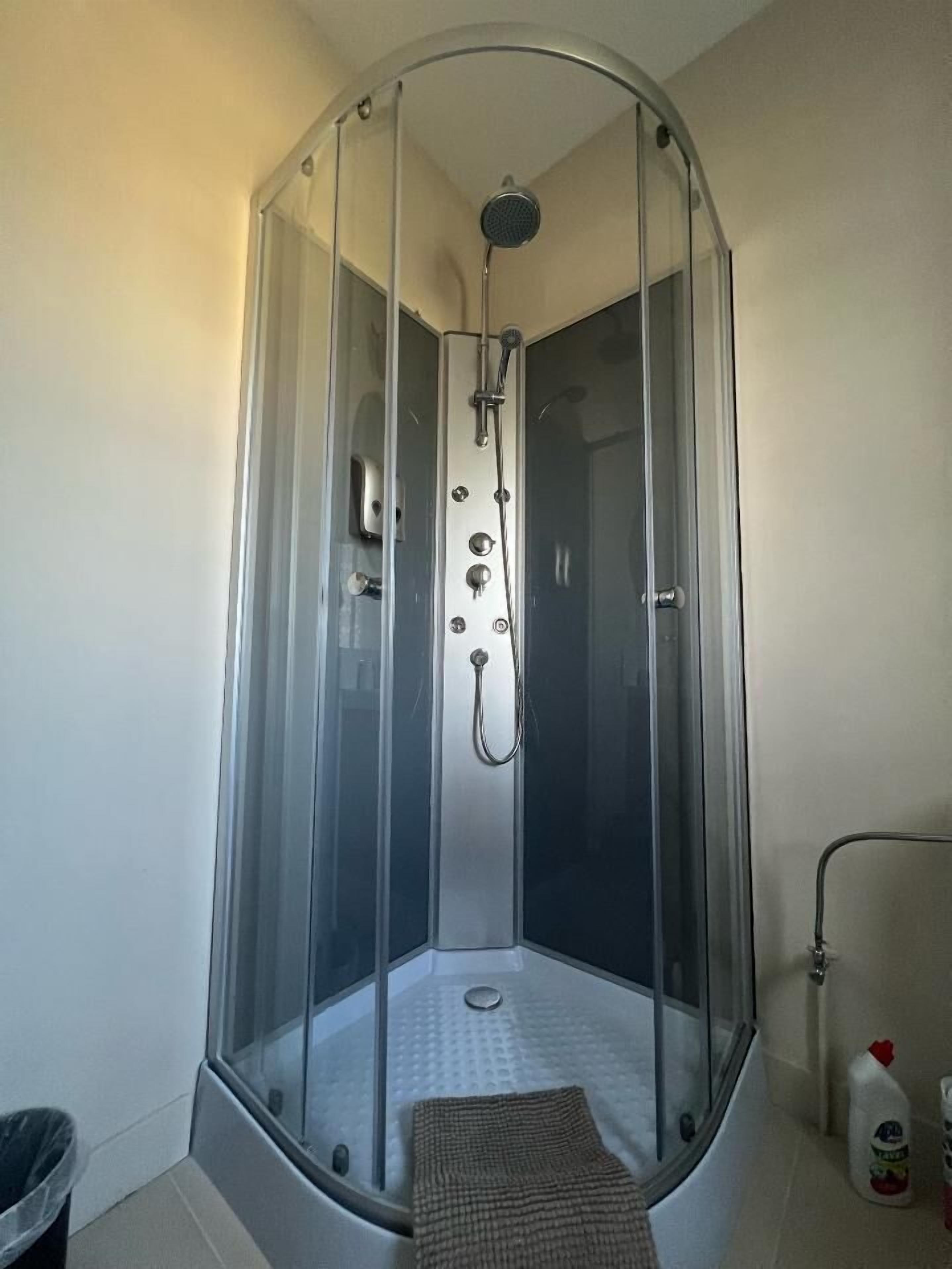 Une cabine de douche fermée par des parois en verre, équipée d’un pommeau de douche à main et d’un flexible de douche à main.