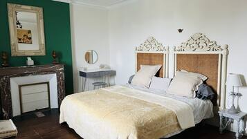 A bedroom with a large bed, a dresser, a vanity, and a fireplace.
