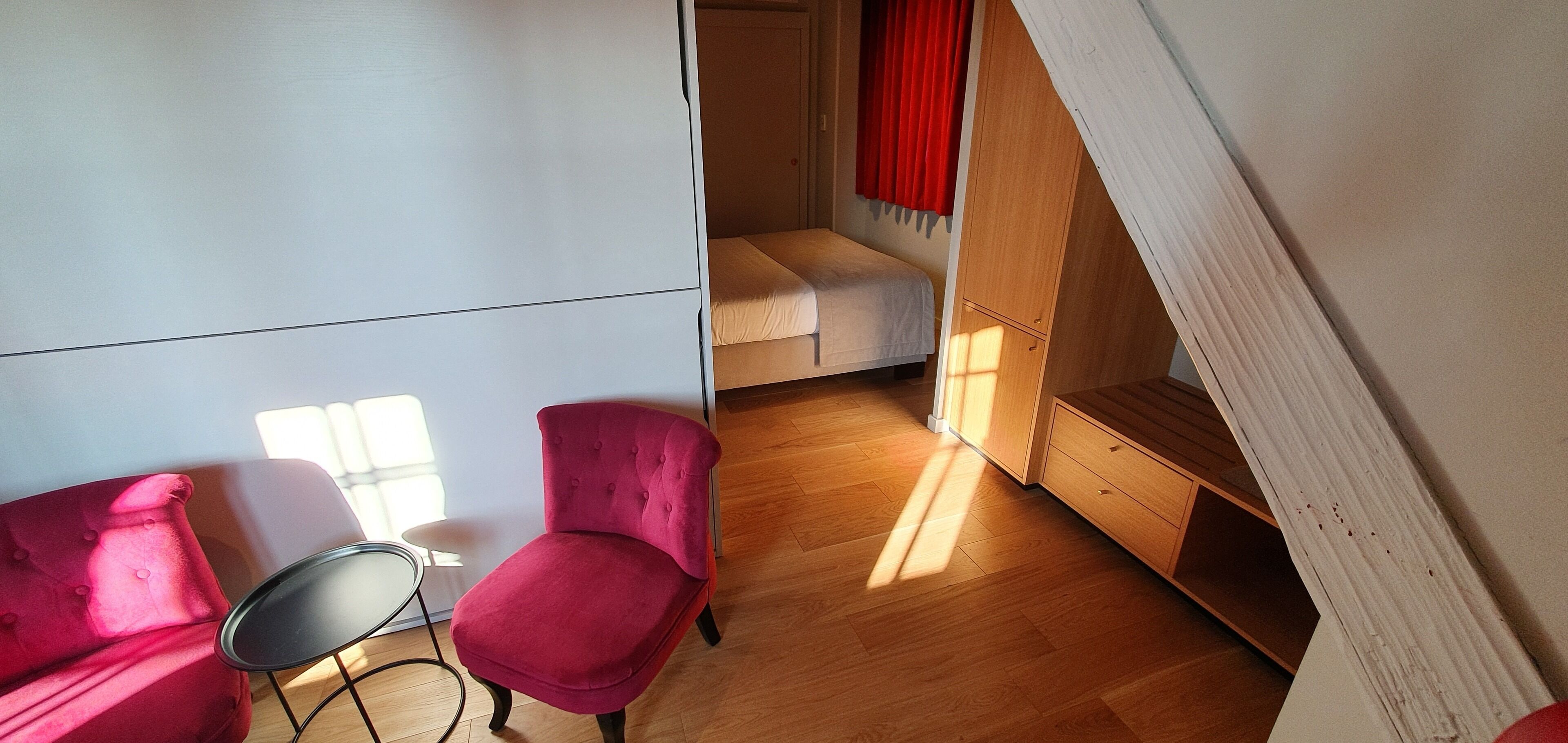 A room with a bed, a red chair, a small table, and a wooden bench.