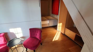 A room with a bed, a red chair, a small table, and a wooden bench.