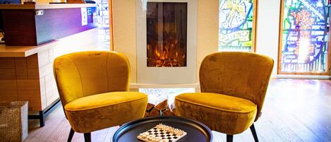 A cozy room with a fireplace, two yellow armchairs, and a chessboard on a small table.