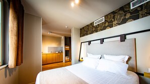 Habitación de hotel con una cama grande, un armario de madera y una pequeña cocina.