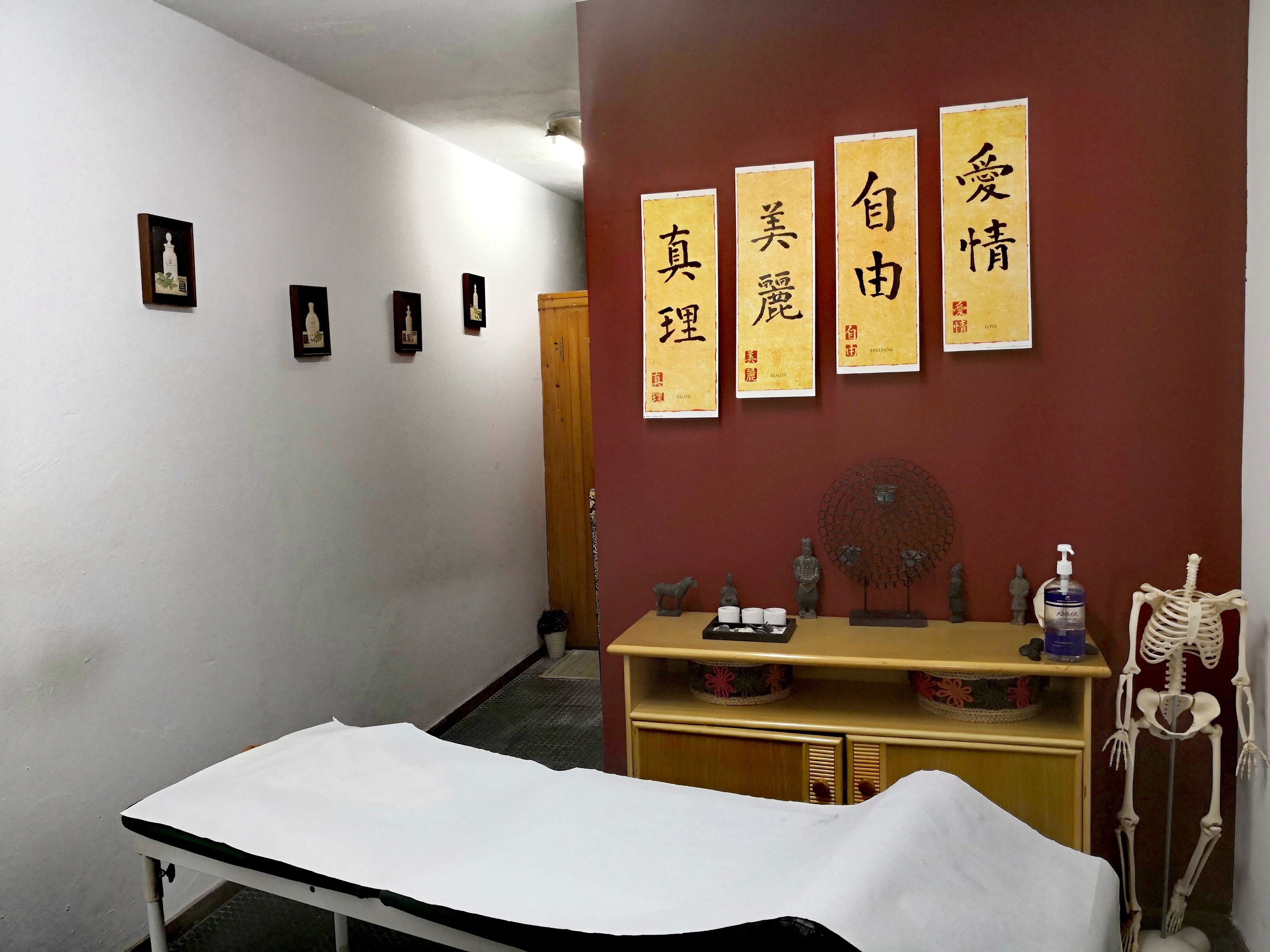A room with a bed, a wooden cabinet, and a wall with four framed calligraphy pieces.