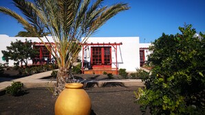 A building with a red door and white walls, surrounded by greenery and a large golden pot. - Bungalows Castillo Club Lake (Antigua)