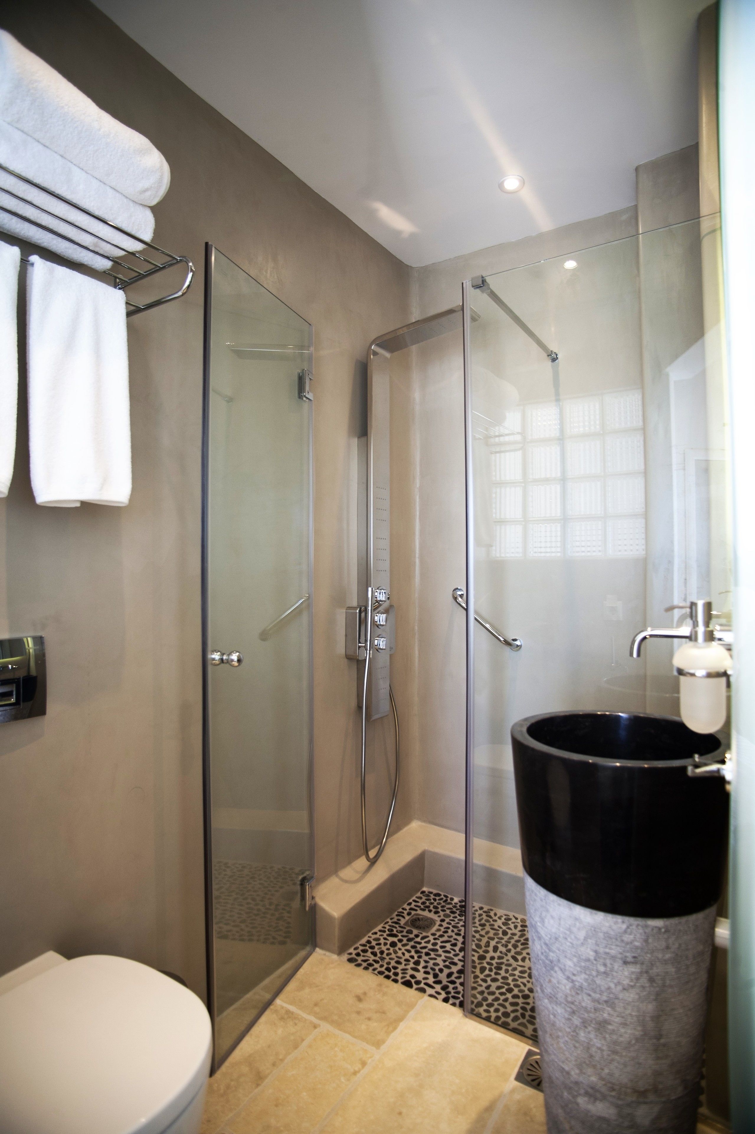 A modern bathroom with a glass-enclosed shower, a toilet, and a large black basin.