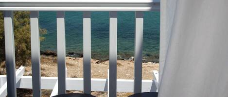 A balcony with white railings and two black cylindrical objects, overlooking a coastal landscape with a lighthouse and boats.