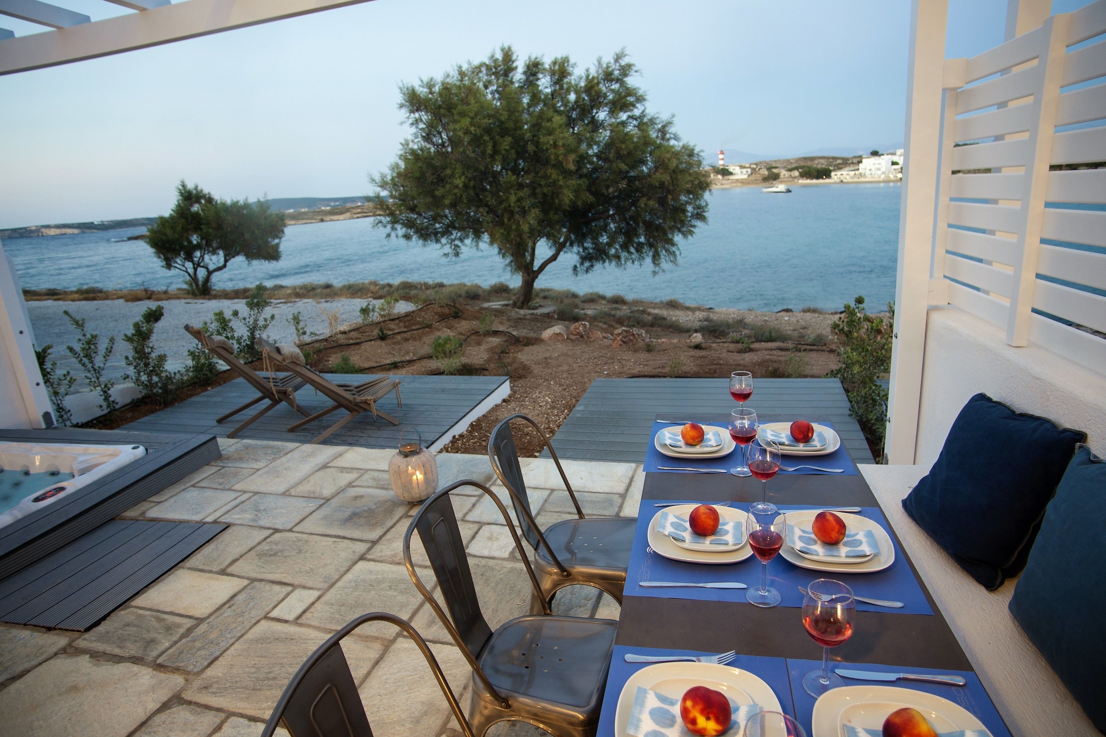 An outdoor dining area with a table set for two, overlooking a body of water and a tree.