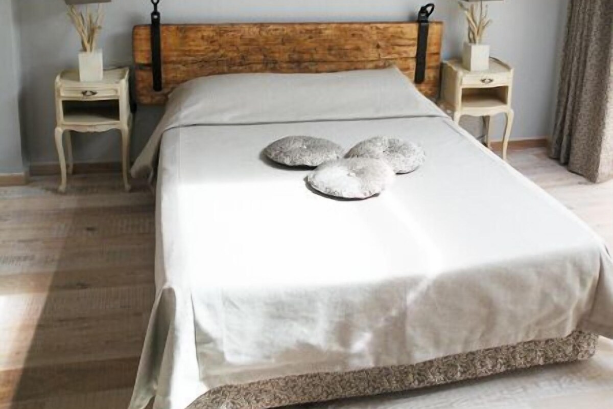 Ein Schlafzimmer mit schrägen Wänden, einem hölzernen Kopfteil, einer Kandelaberleuchte, Nachttischlampen und einem Bett mit Kissen.