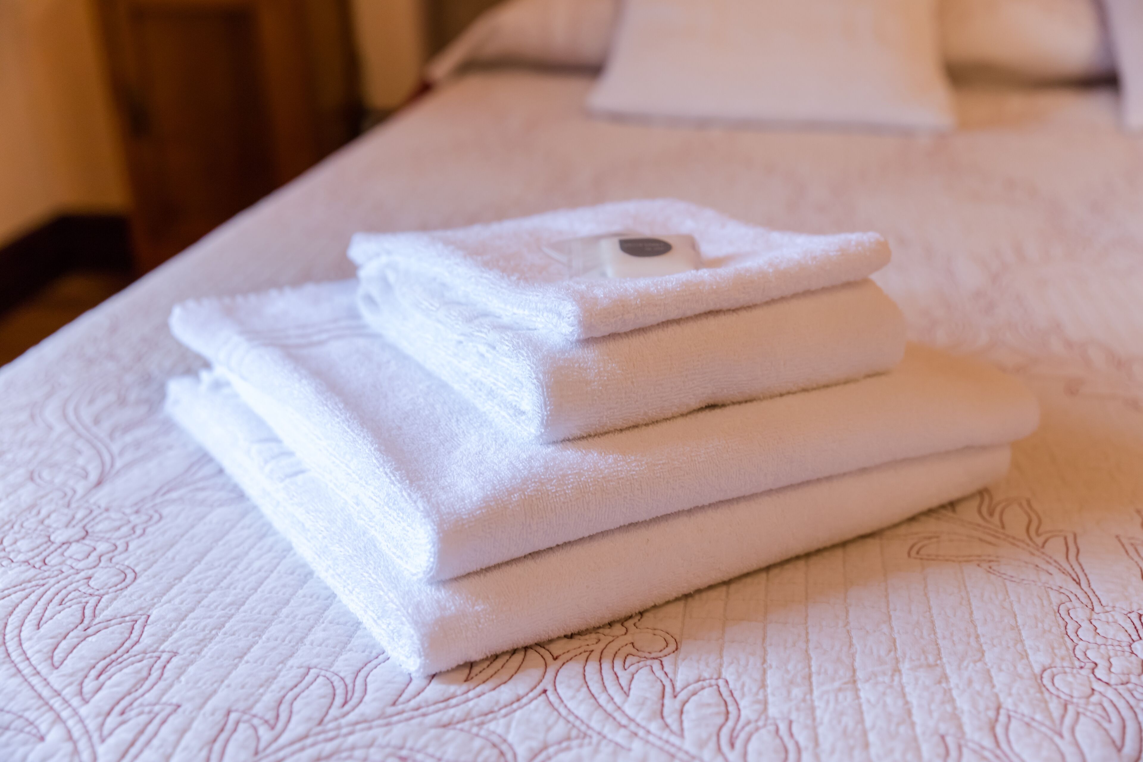 Une pile de serviettes blanches, soigneusement pliées, est posée sur un lit recouvert d’une couvre-lit à motifs floraux.