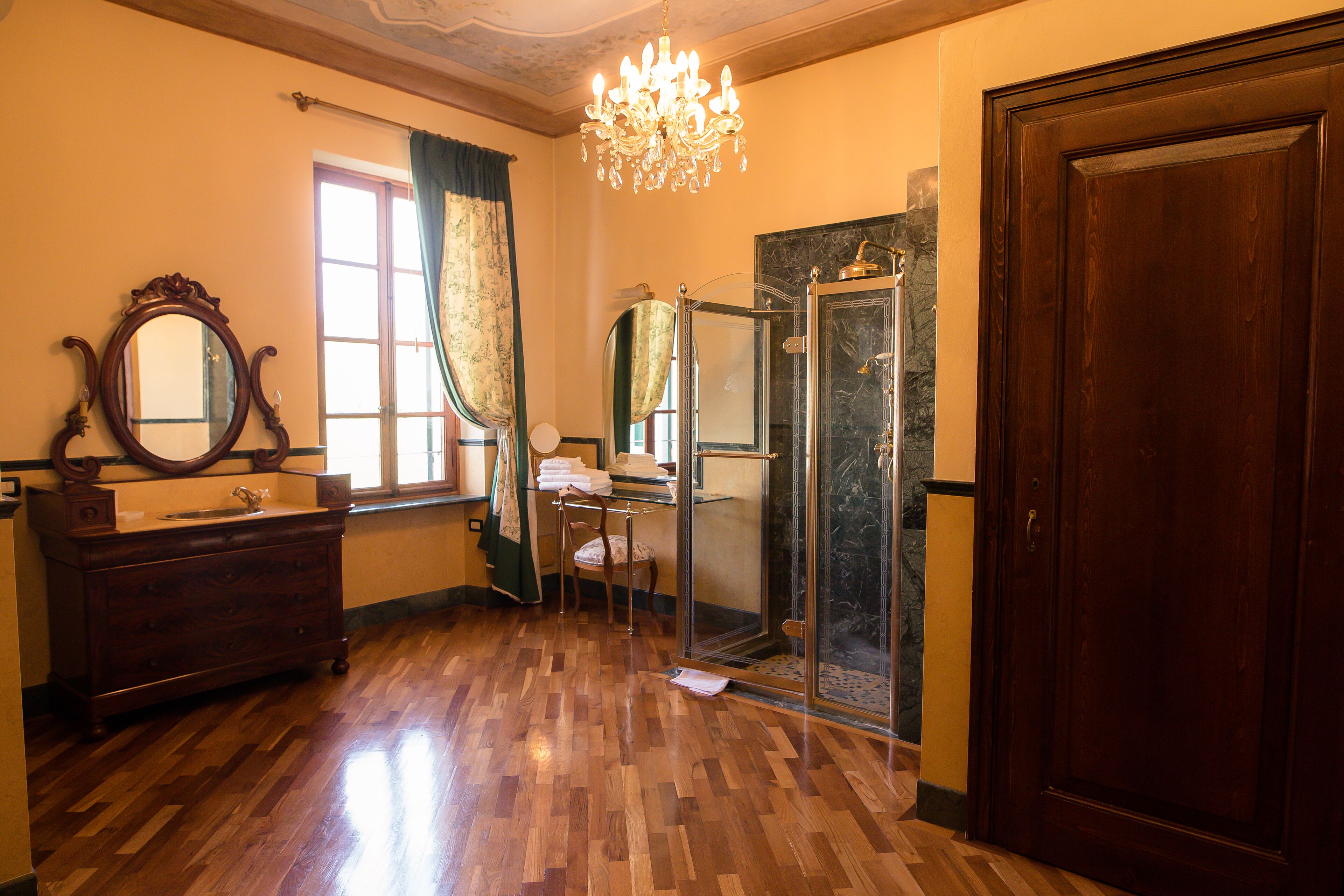 A room with a wooden dresser, a mirror, a chandelier, a shower, and a door.