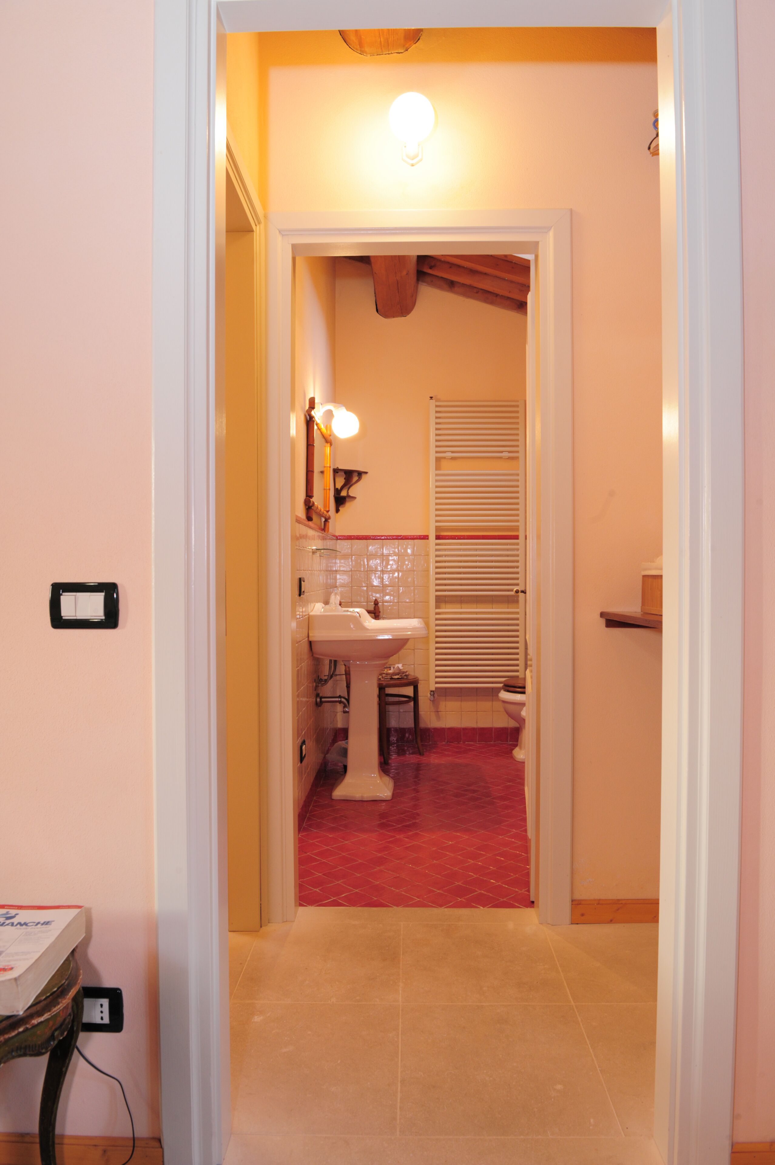 A narrow hallway with a red carpet leading to a bathroom with a sink, mirror, and toilet.