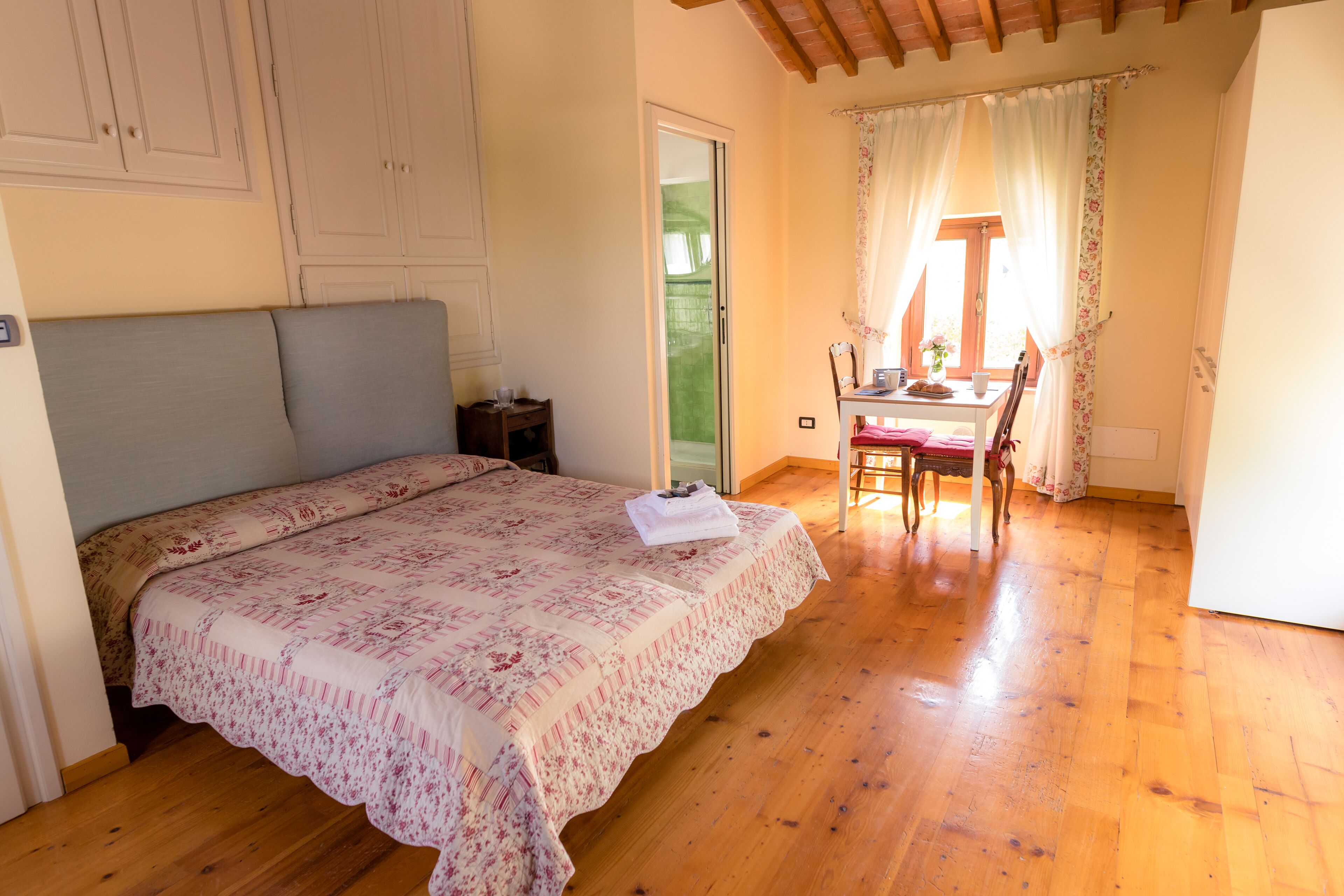 Ein Schlafzimmer mit einem Bett, Holzboden, einem Schreibtisch mit Stuhl und einem Fenster mit Vorhängen.