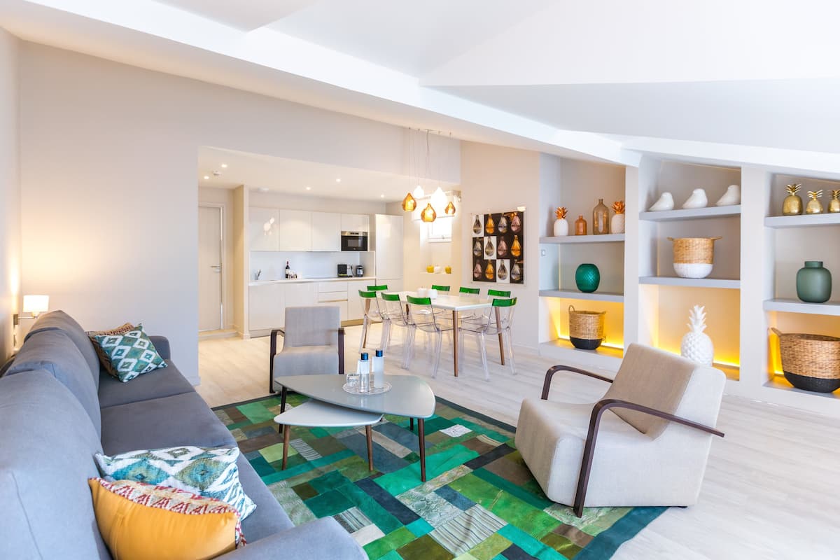 Un salon moderne avec un canapé gris, une table basse et un coin repas comprenant une table et des chaises blanches.