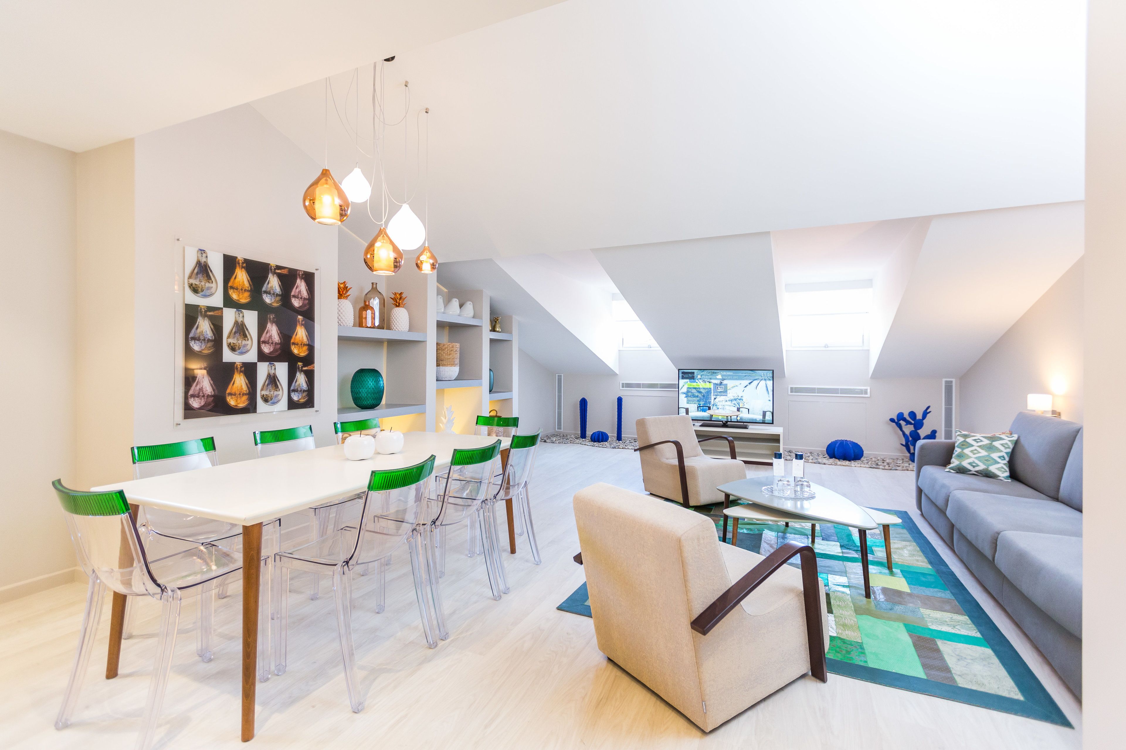 Una sala de estar moderna con comedor, que presenta una mesa blanca, sillas transparentes y un sofá gris.