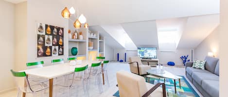 Una sala de estar moderna con comedor, que presenta una mesa blanca, sillas transparentes y un sofá gris.