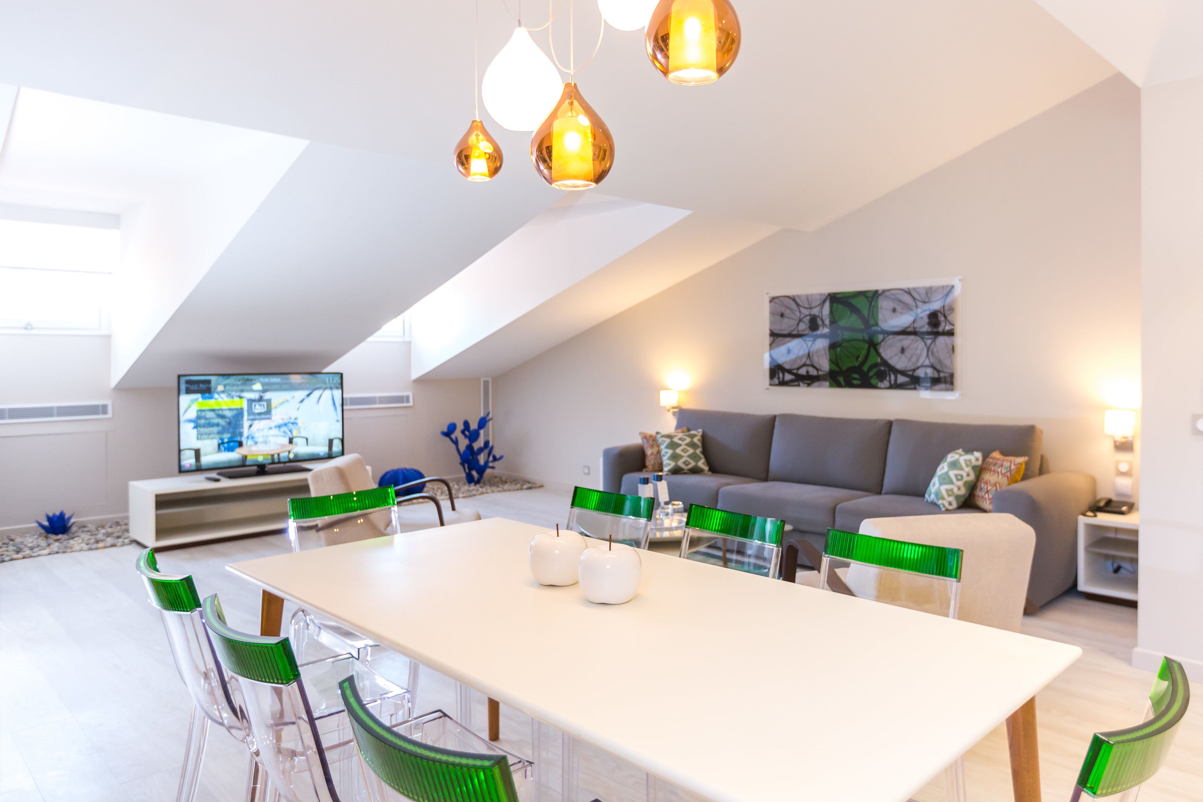 A modern living room with a dining area, a grey sofa, and a flat-screen TV.