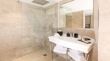 A modern bathroom with a glass-enclosed shower, a white sink with a mirror, and neatly stacked towels.