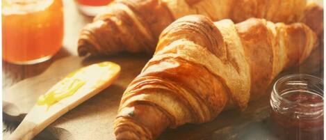 Dos croissants sobre una tabla de madera con un cuchillo y un tarro de mermelada.