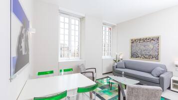 A modern living room with a white table, green chairs, a grey sofa, and a large abstract painting on the wall.