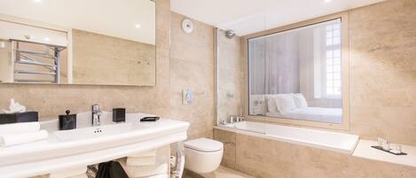 A modern bathroom with a large mirror, a white sink, a toilet, and a bathtub.