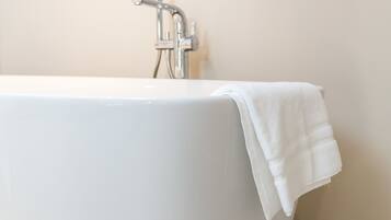 A white bathtub with a towel on it, set against a plain wall and a tiled floor.