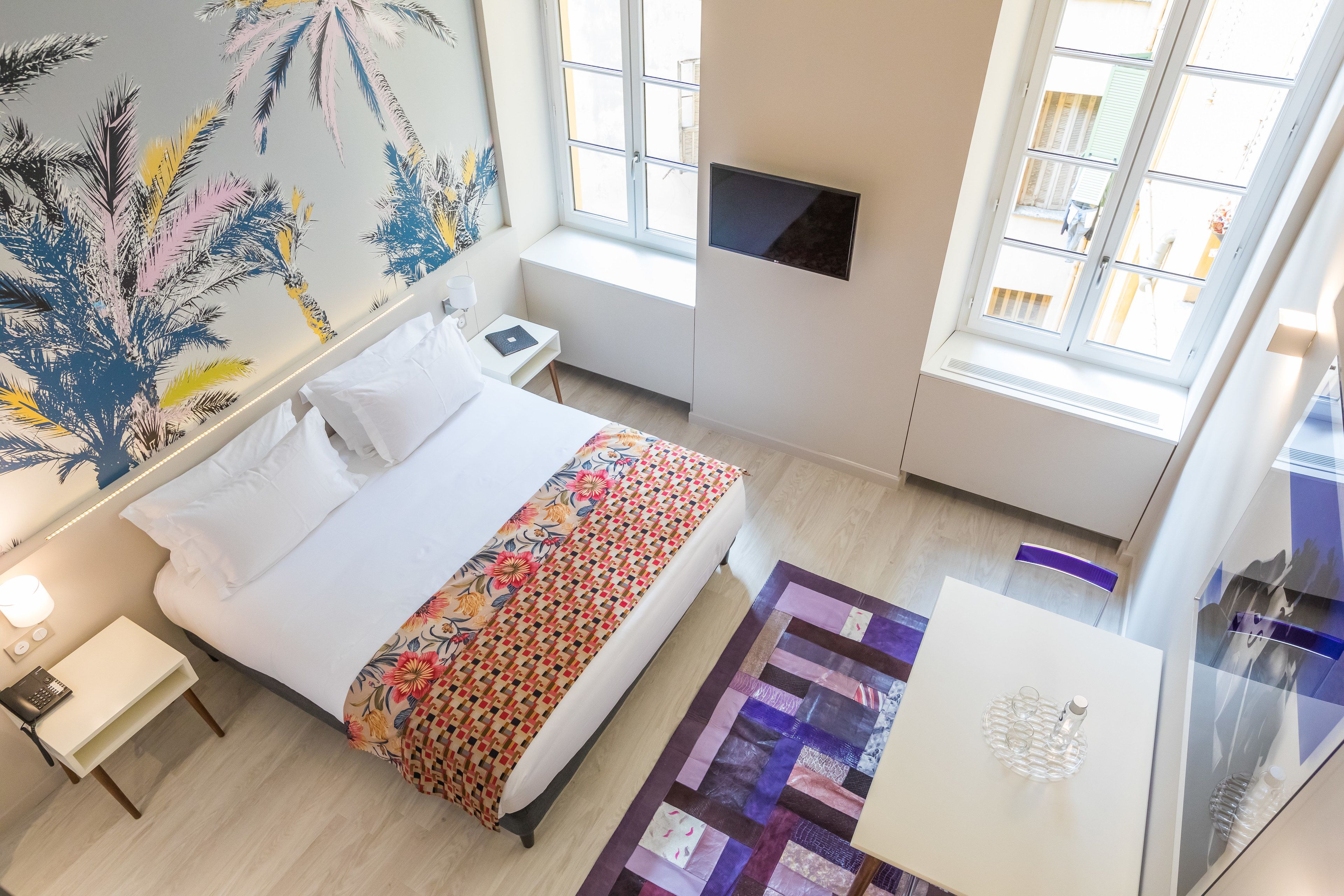 A bedroom with a bed, bedside table, nightstand, and a wall-mounted TV.