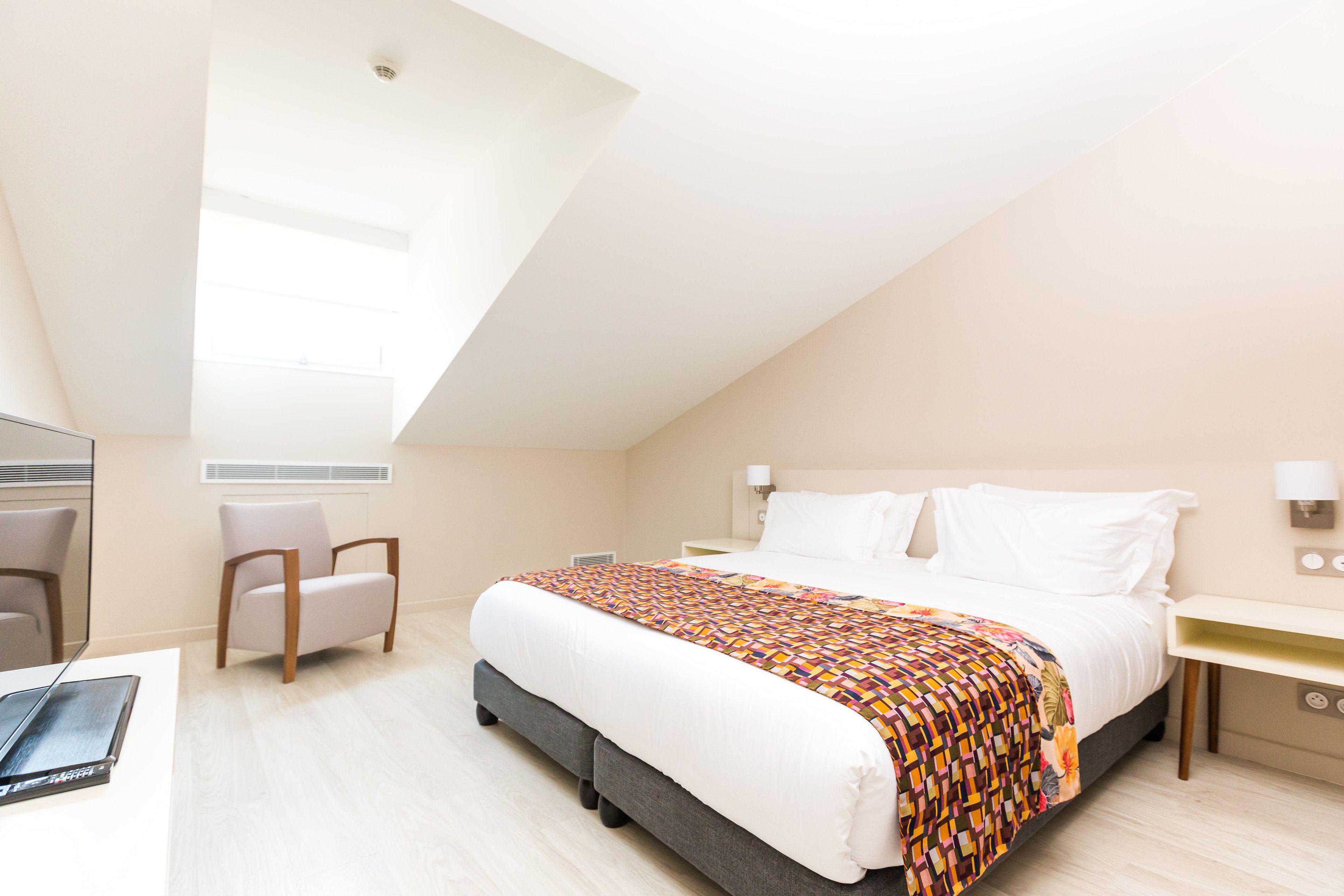Una habitación de hotel moderna con una cama grande, un escritorio, una silla y un tragaluz.