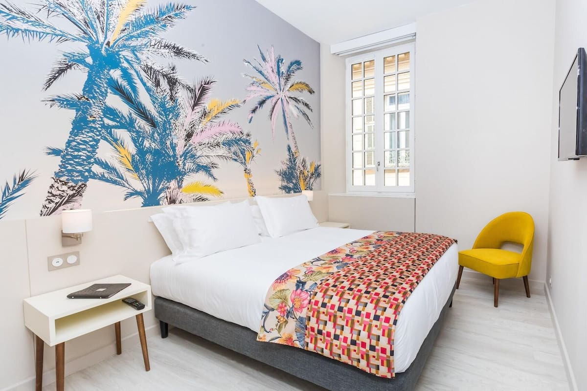 Une chambre d’hôtel avec un lit, un bureau, une chaise, une décoration murale et une fenêtre.