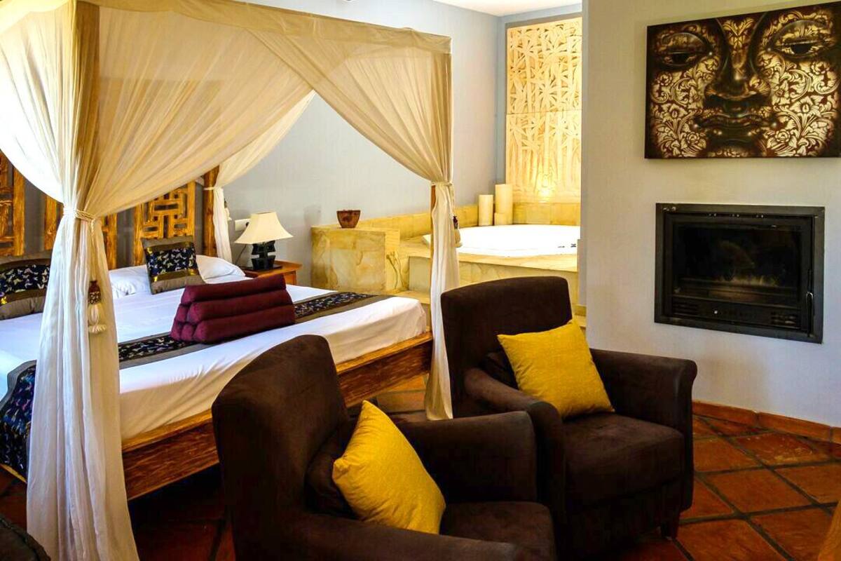Un dormitorio con cama con dosel, chimenea y dos sillones con cojines amarillos.