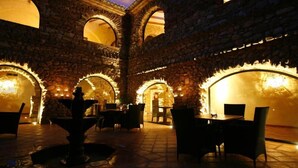 Un patio interior con muros de piedra, arcos y mesas y sillas dispuestas para comer.