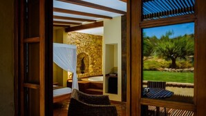 Una habitación con pared de piedra, un ventanal grande, una silla de mimbre y vistas a un jardín.
