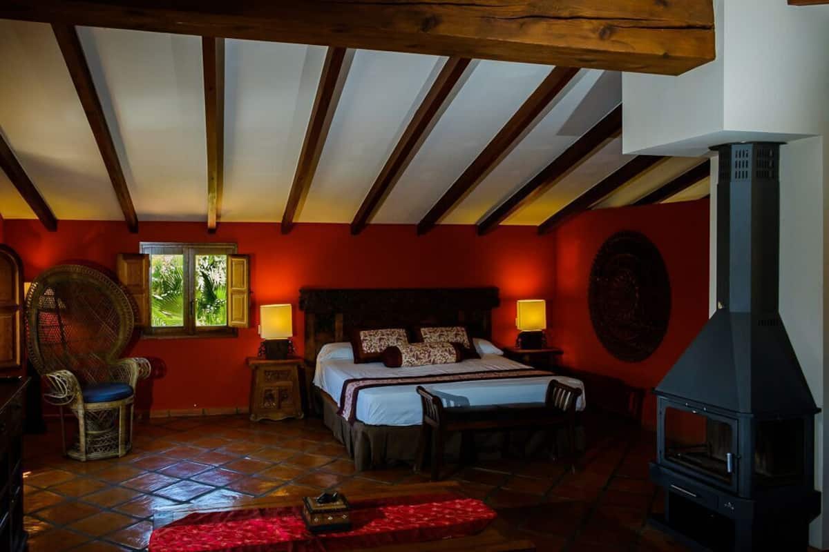 Una habitación con cama, vigas de madera, chimenea y ventana con vistas al verdor.