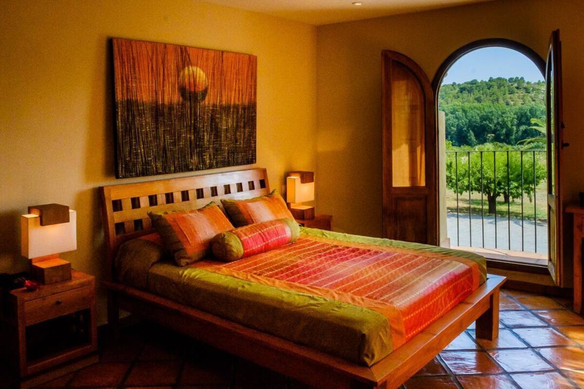 Un dormitorio con una cama grande, una mesita de noche, un cuadro en la pared y vistas a un jardín a través de una puerta.