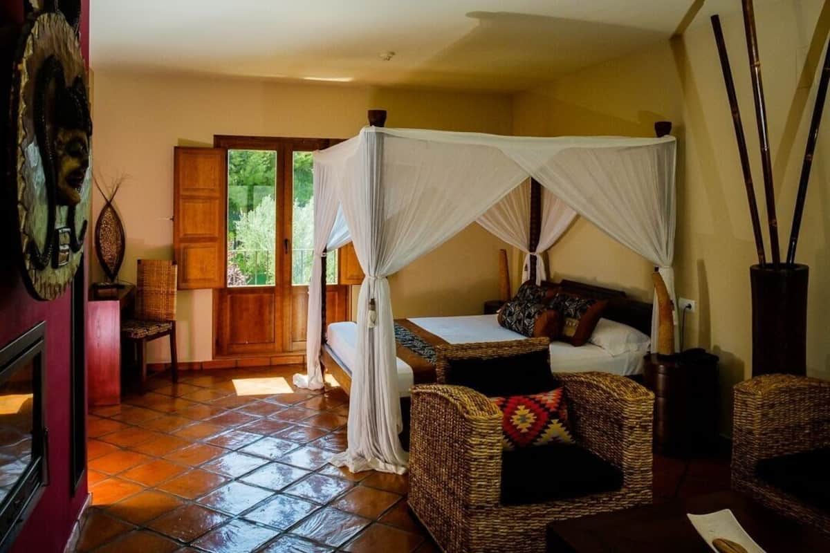 Una habitación con una cama bajo dosel, muebles de mimbre y vistas al exterior.
