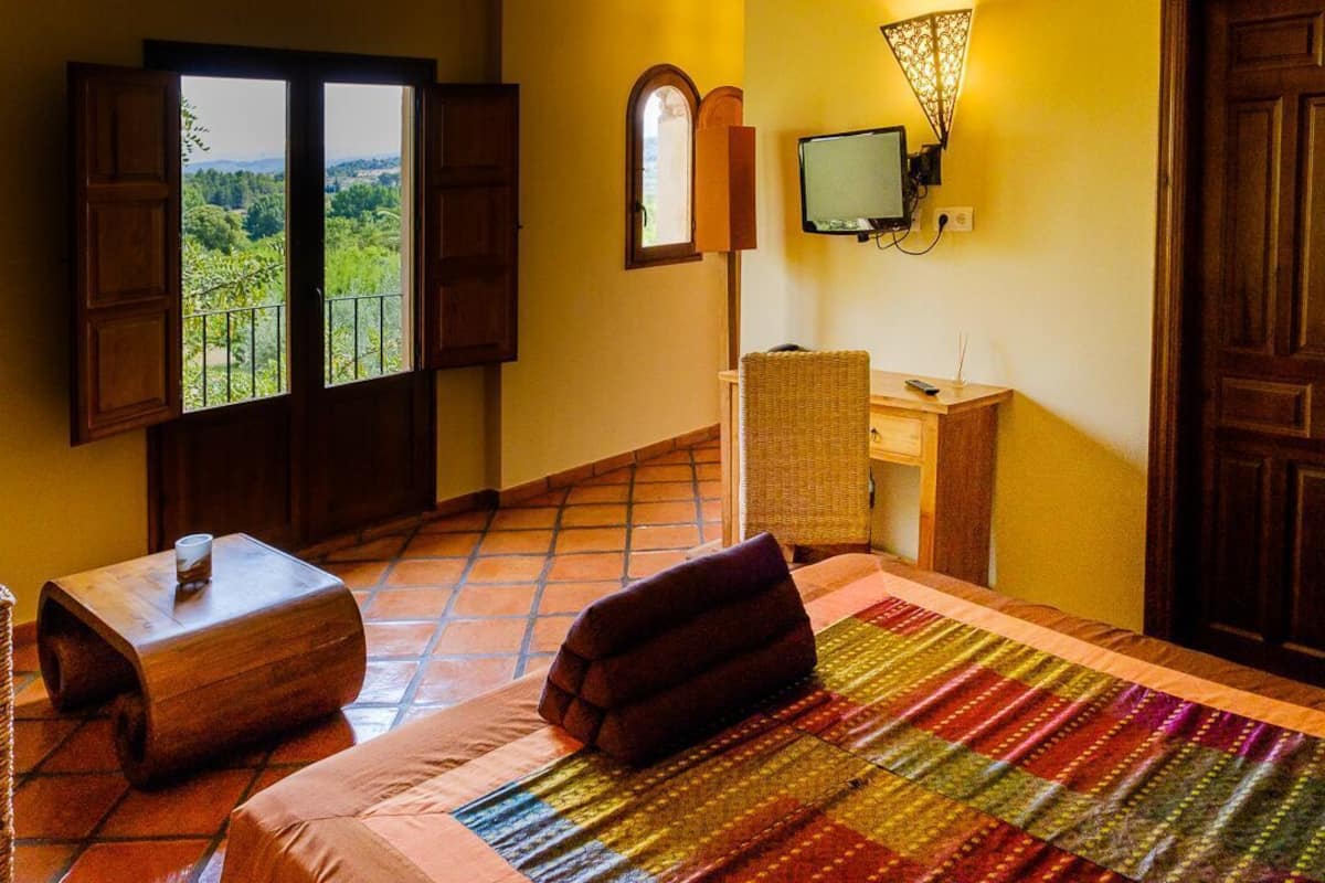 Una habitación con cama, una mesita pequeña, un escritorio, televisor y ventana con vista a la vegetación.
