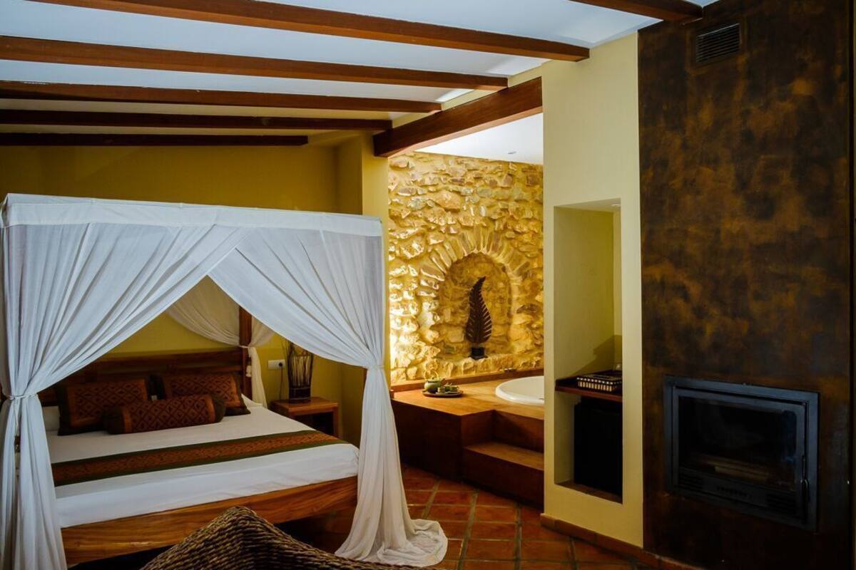 Una habitación con cama bajo dosel, pared de piedra, bañera y chimenea.