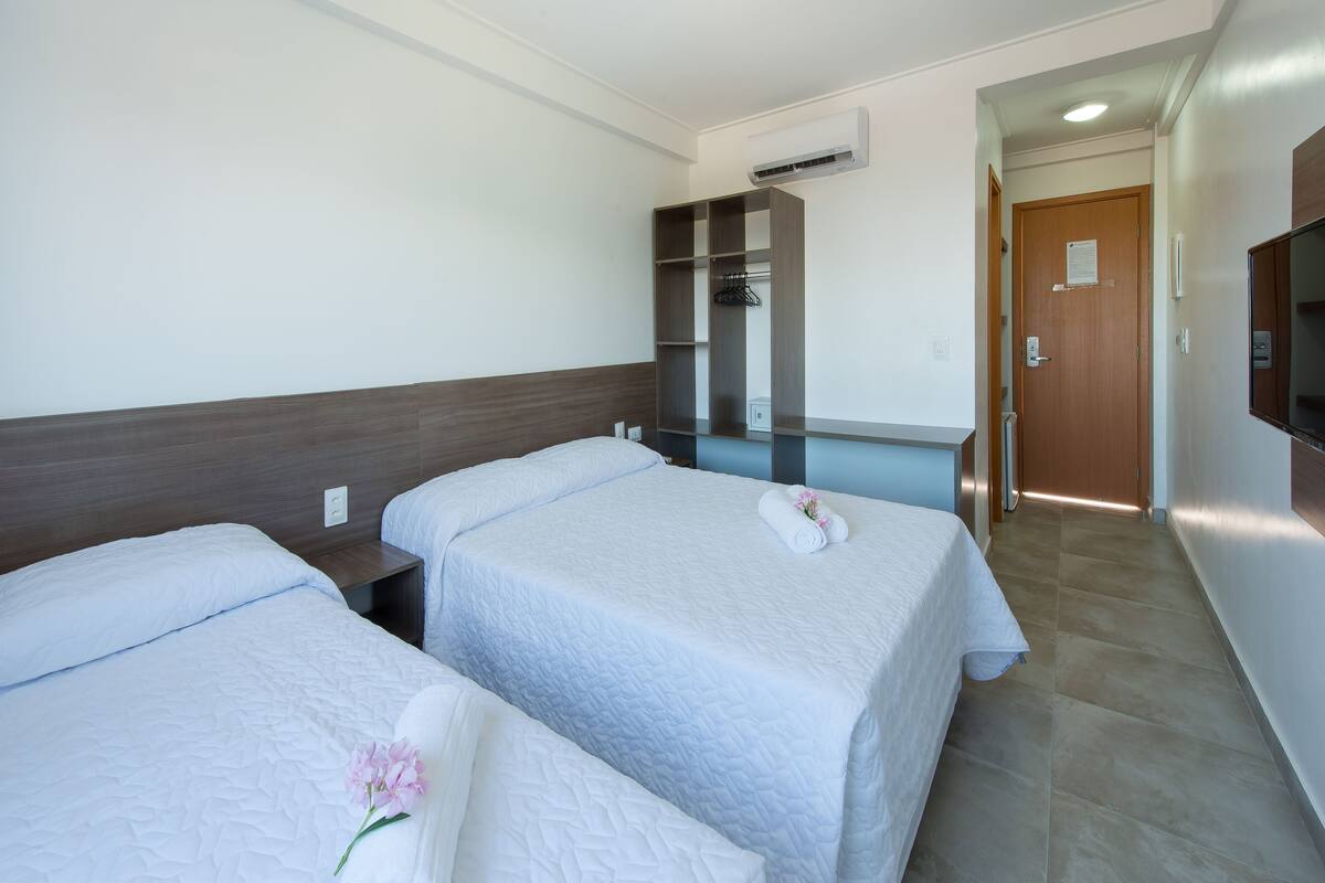 Een hotelkamer met twee bedden, een kledingkast, een televisie en een airconditioning.