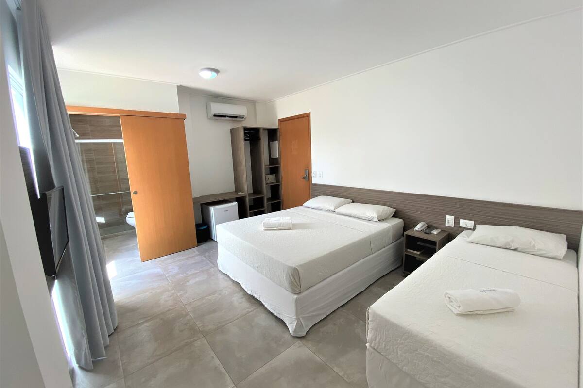 Een hotelkamer met een groot bed, een kleiner bed, een bureau, een kledingkast en een badkamer die door een open deur zichtbaar is.