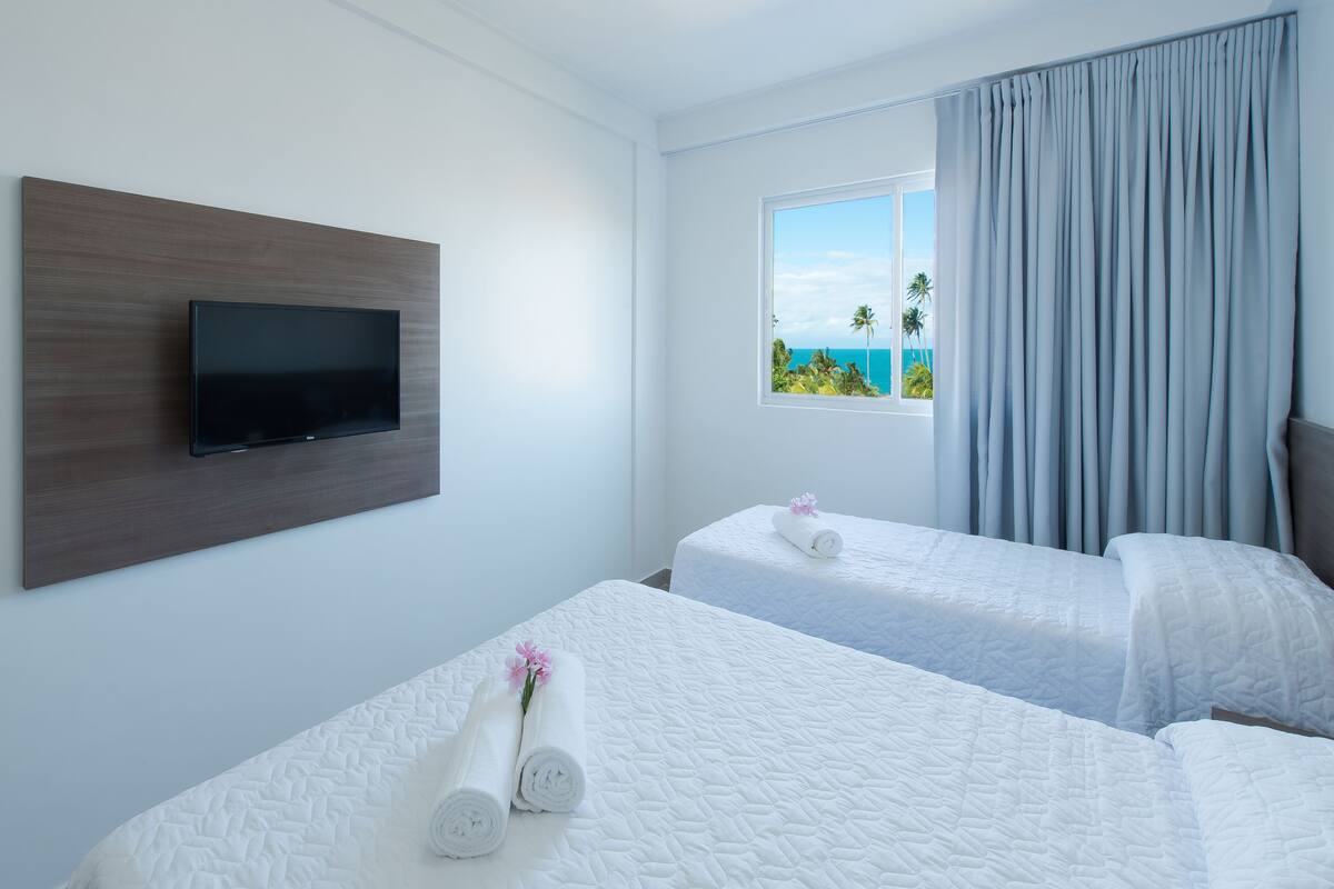 Een hotelkamer met twee bedden, een flatscreen-tv aan de muur en een raam met uitzicht op de oceaan.
