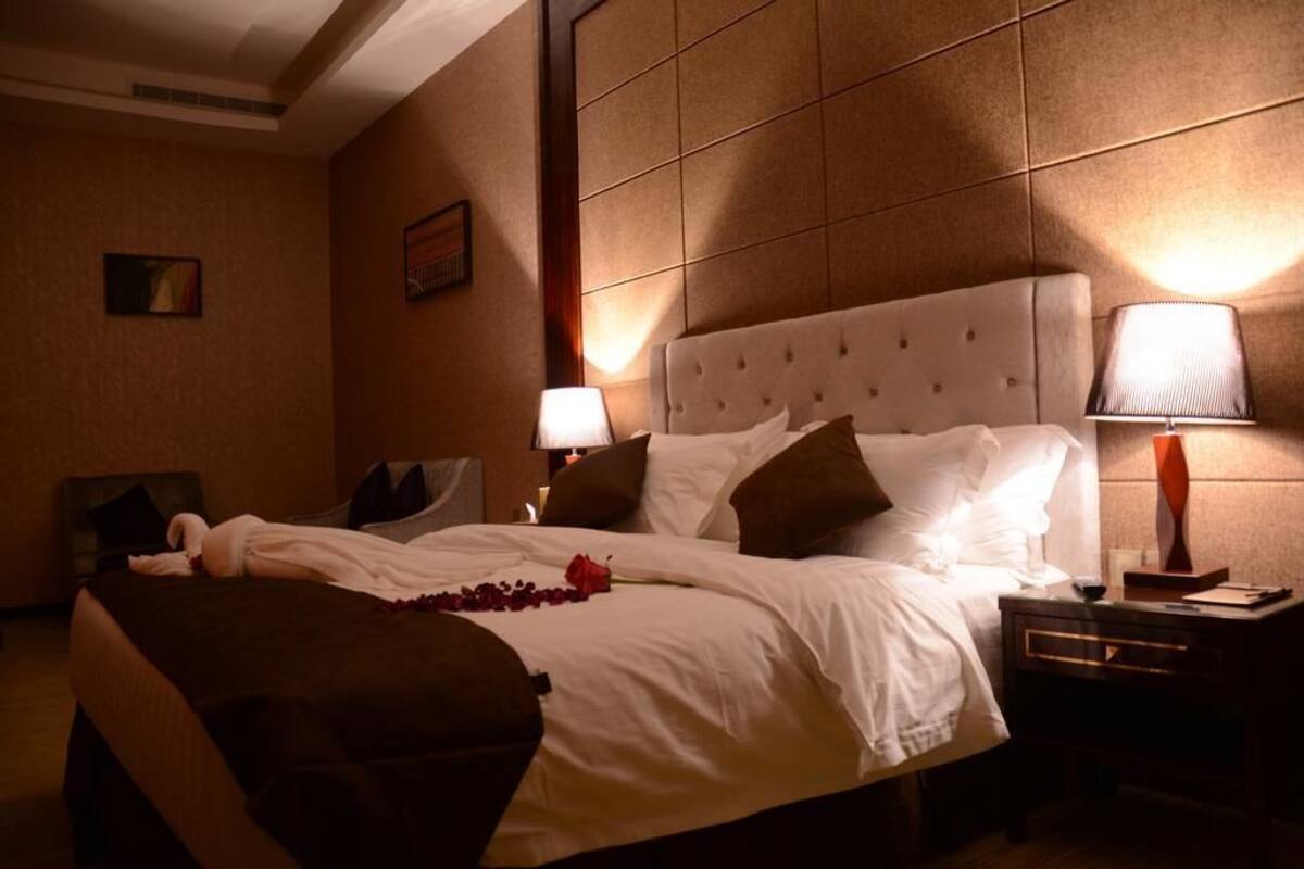 A hotel room with a large bed, a bedside table with a lamp, and a headboard with a tufted design.