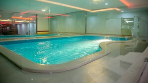 An indoor swimming pool with clear water, surrounded by glass walls and a tiled floor. - Seven Garden AL wadi (Riyadh)