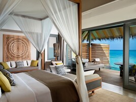Un dormitorio con una cama grande, una zona de estar con vistas al océano y una decoración temática tropical.