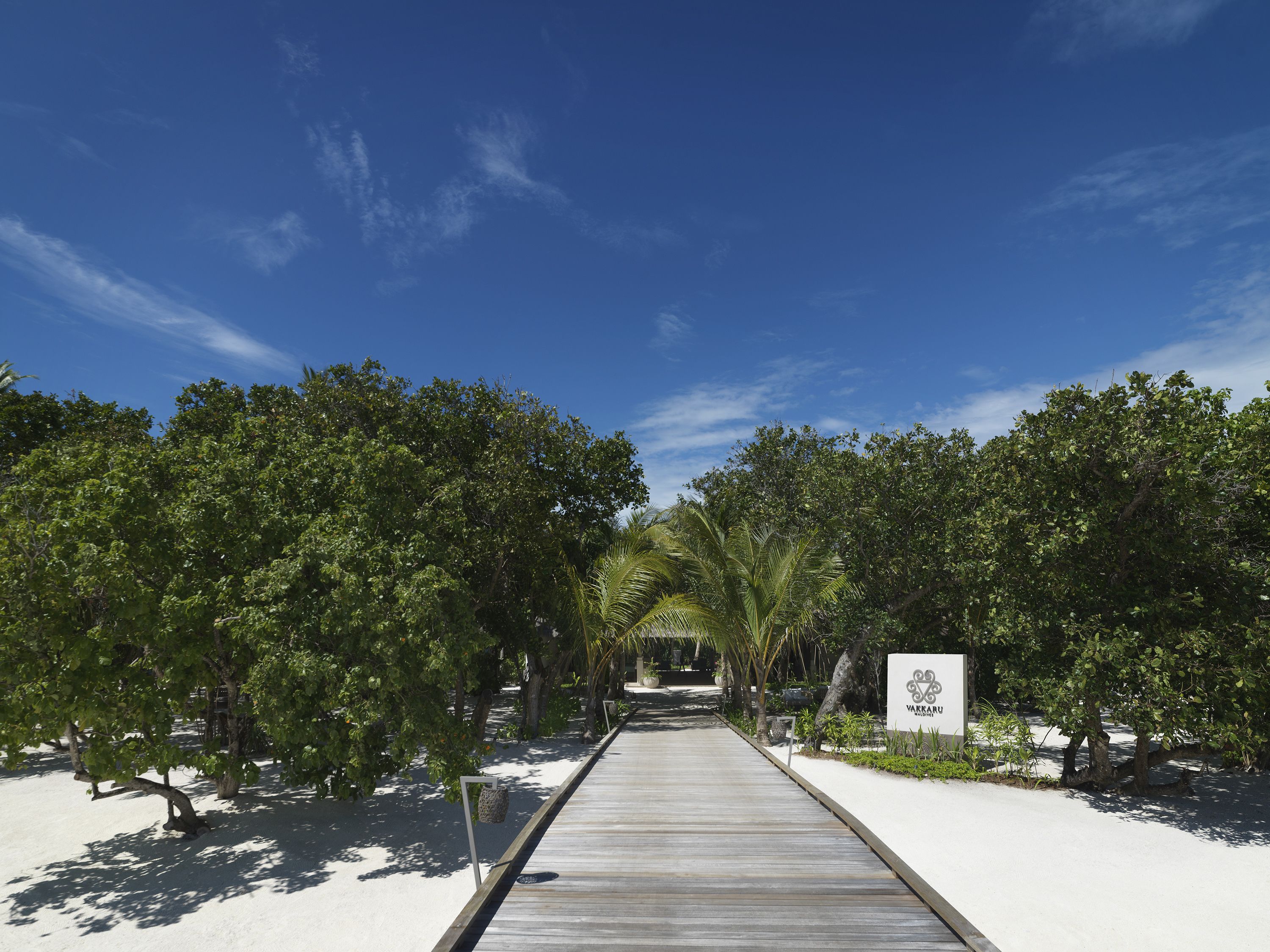 Un sendero de madera que atraviesa un jardín tropical, con un cartel que indica un centro de spa o bienestar.
