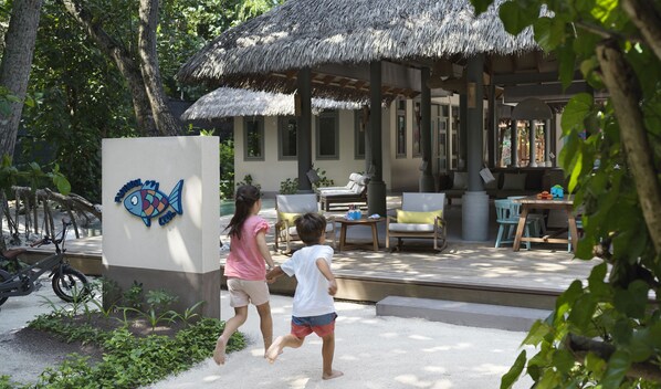 Un resort tropical con un pabellón de techo de paja, mobiliario exterior y un cartel con diseño de pez.