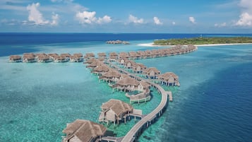 An aerial view of overwater bungalows connected by a wooden walkway.