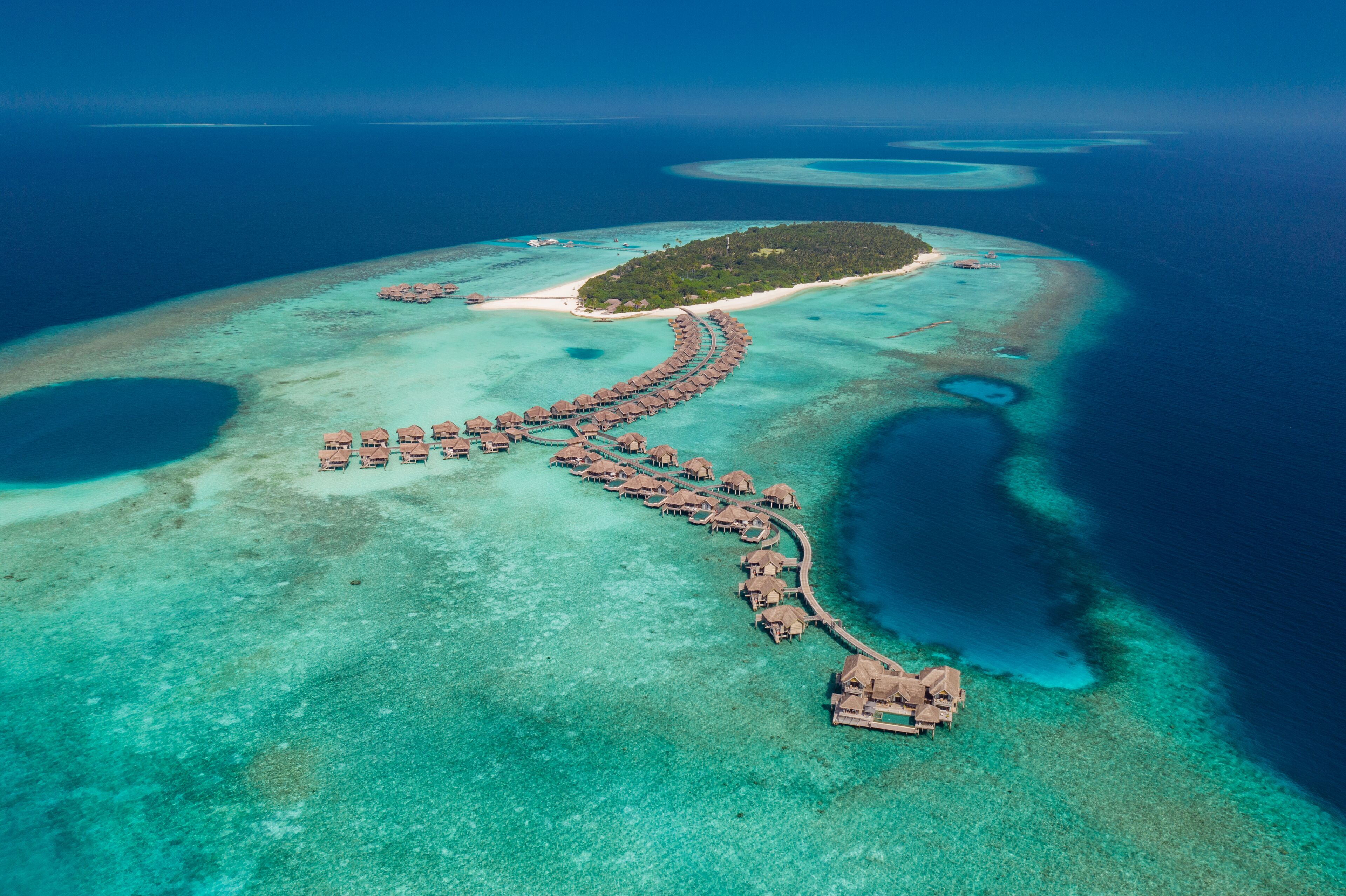 Vista aérea de un resort sobre el agua, con un muelle largo que conecta con bungalows sobre el agua.