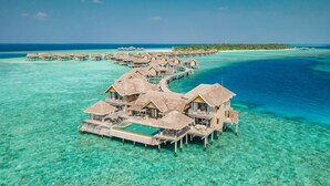 Des bungalows sur pilotis dotés d’une piscine, reliés par des passerelles, au-dessus d’une mer turquoise et cristalline.