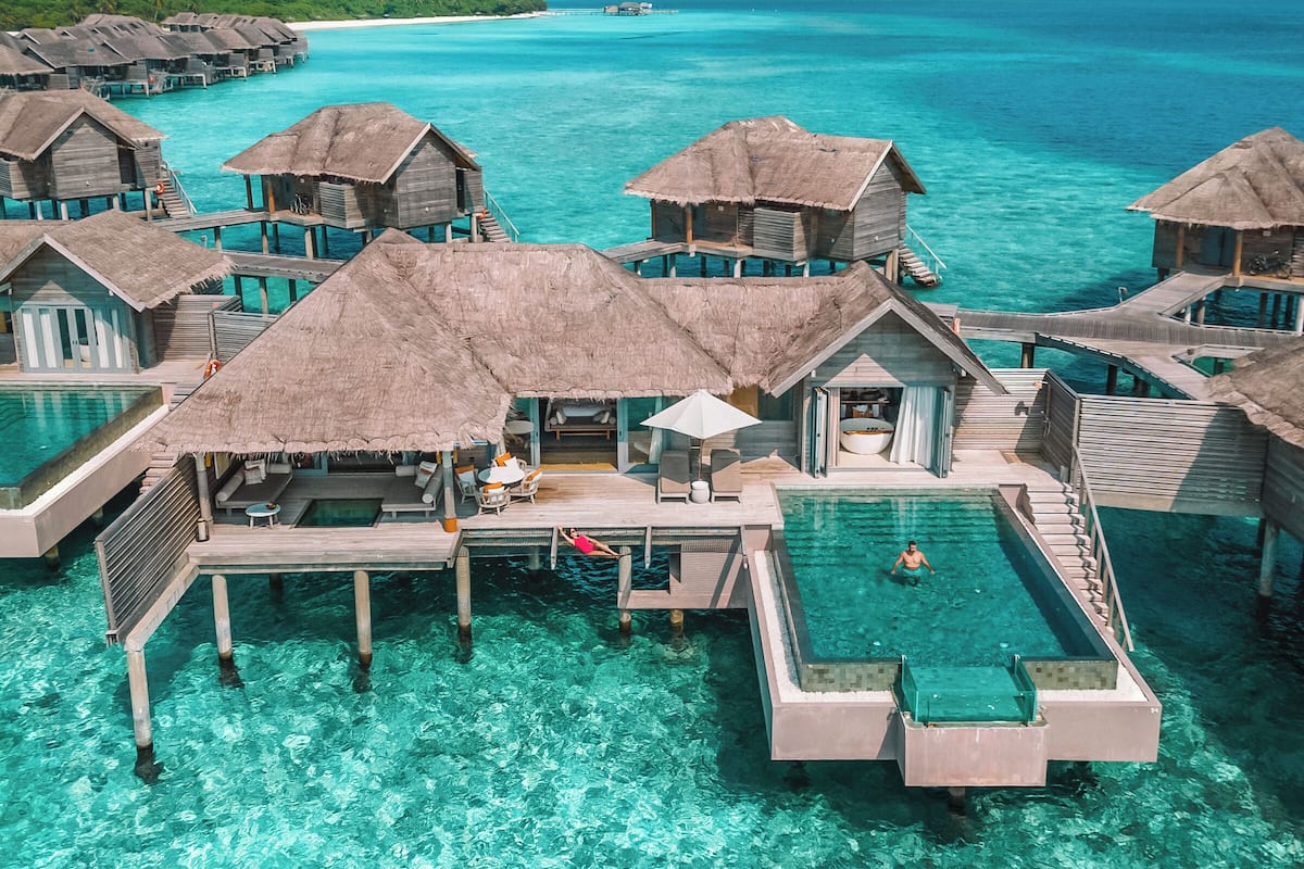 Bungalows sobre el agua con piscinas infinitas, agua turquesa cristalina y vista al océano.